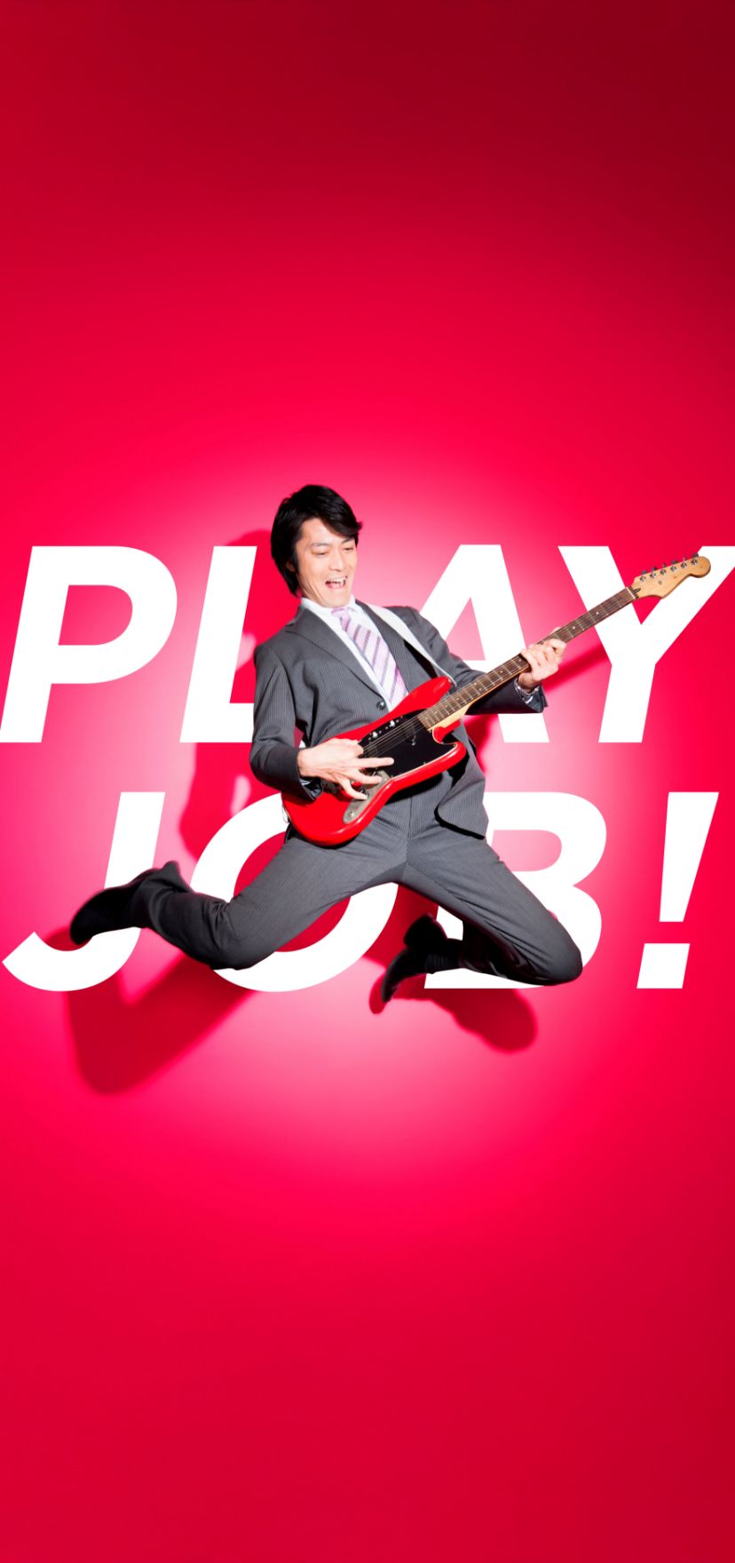 「PLAY JOB!」の文字を背景に、スーツ姿でエレキギターを弾きながらジャンプする男性